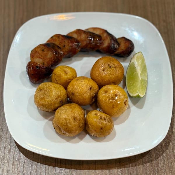 Grilled sausage slices, small golden potatoes, and a lime wedge on a white plate.