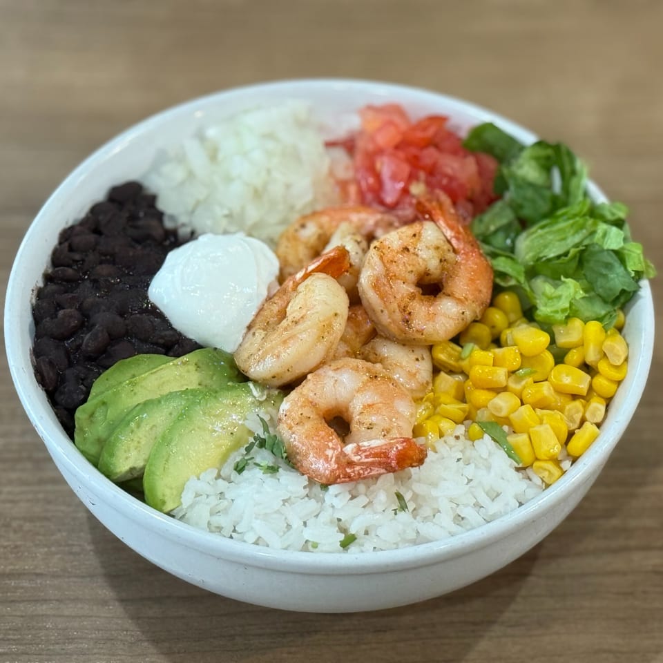 A Nazca Express shrimp bowl with rice, black beans, avocado, corn, tomatoes, lettuce, and sour cream.