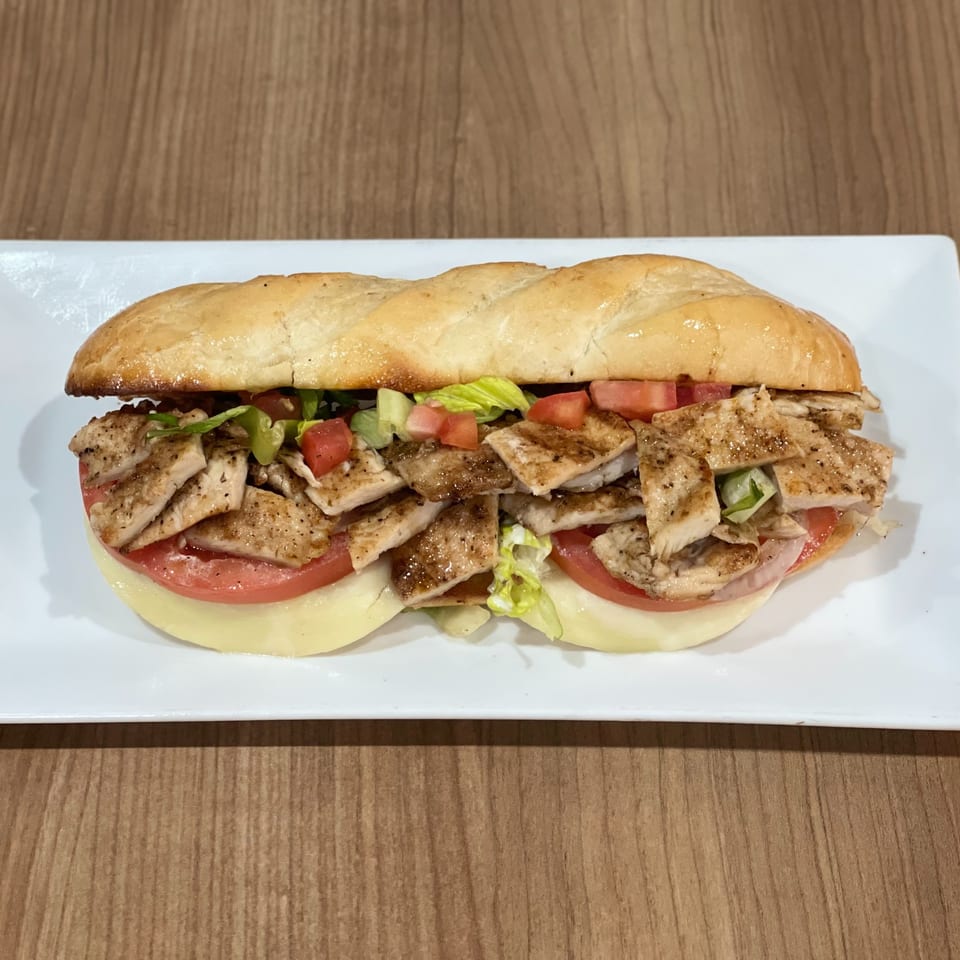 A Nazca Express chicken sandwich with lettuce, tomatoes, and cheese on a white plate.