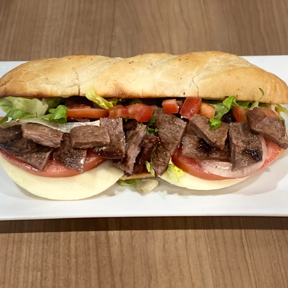 Nazca Express steak sandwich with lettuce, tomatoes, onions, and cheese on a white plate.